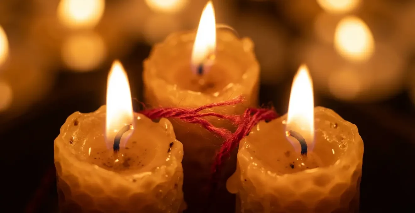 Tres velas encendidas formando un triángulo sagrado con hilo rojo cortado entre ellas